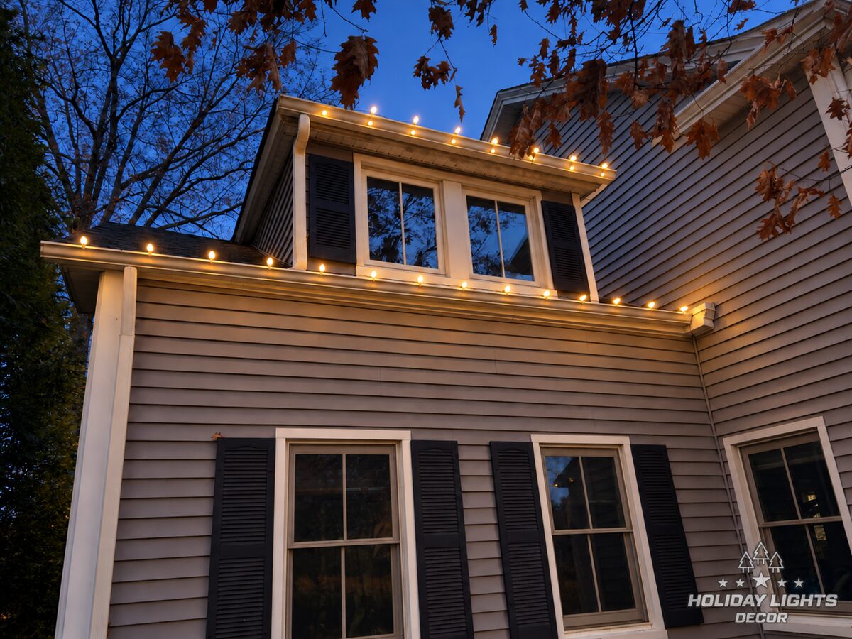 Warm-white bulbs at dusk along a side roof section and upper eave above black-shuttered windows.