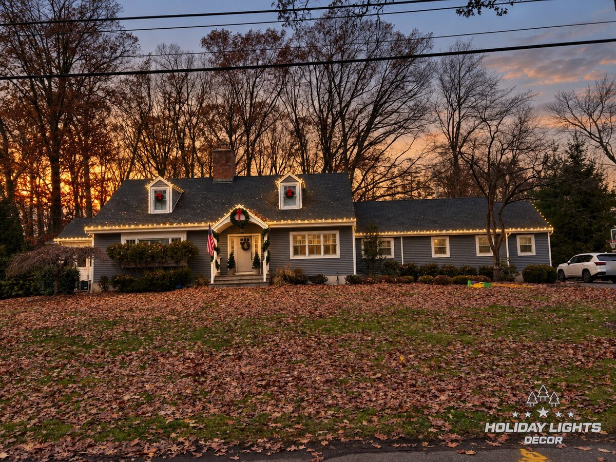 Cape Cod in Wyckoff with warm-white roofline lights, red-bow wreaths on the dormers and front door, and garland on the entry posts
