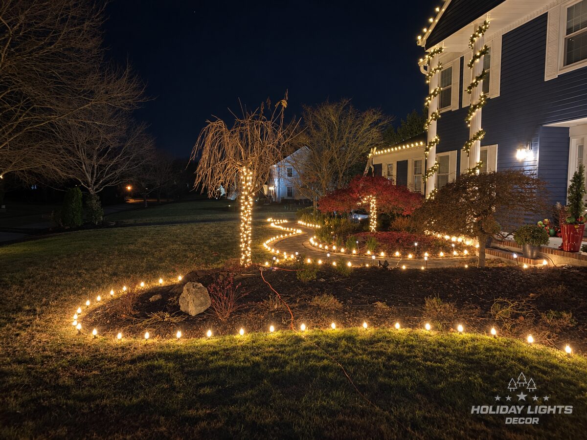 Lit garland wraps tall porch columns beside a curved walkway bordered with warm-white lights