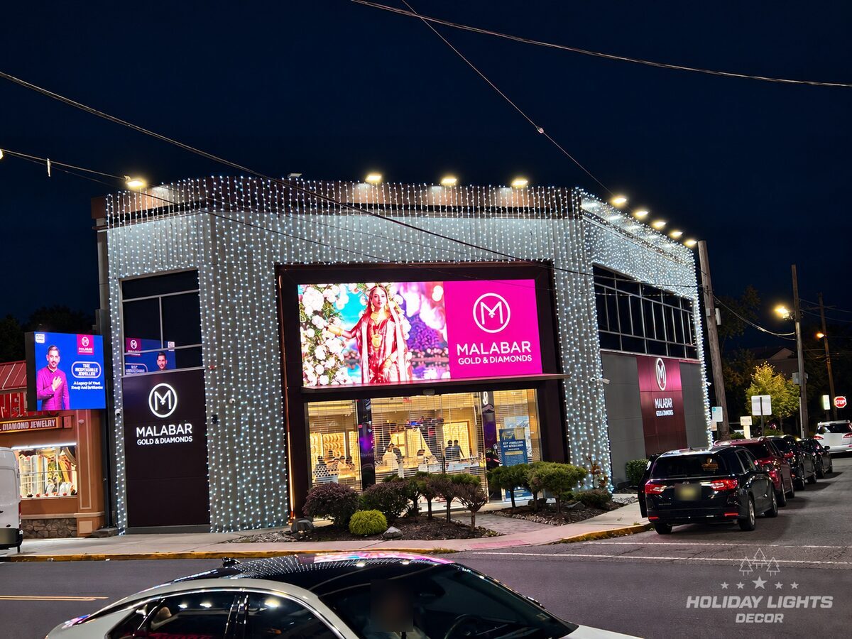 Malabar Gold & Diamonds storefront in Iselin, NJ at night, with cascading cool white curtain lights across the upper façade and corner columns